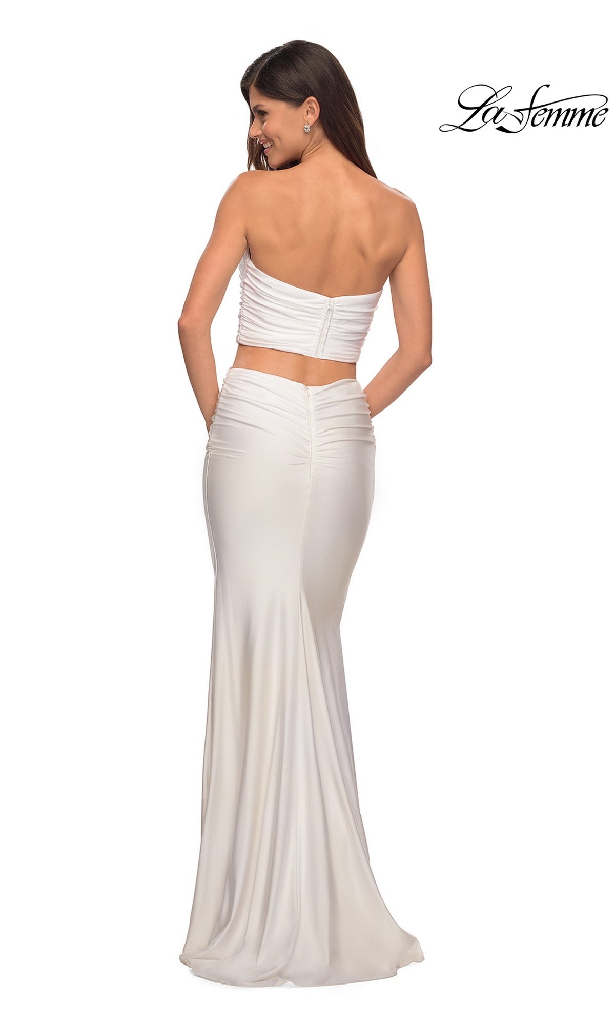 Woman wearing Long Prom Dress: La Femme 28703, a strapless white two-piece with fitted top and sheath skirt, back to camera. “La Femme” logo in top right.
